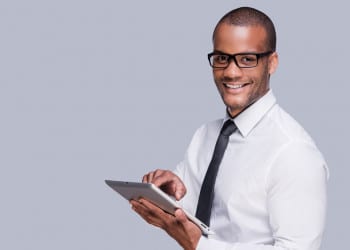 Businessman with digital tablet. Confident young African man in shirt and tie working on digital tablet and smiling while standing against grey background